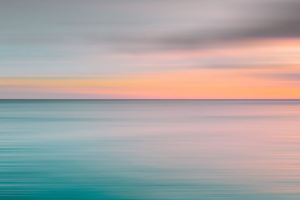 Tranquil ocean view during sunset with soft pastel colors over the horizon.