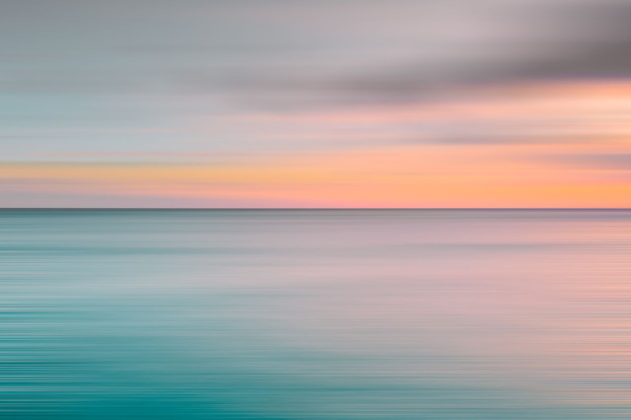 Tranquil ocean view during sunset with soft pastel colors over the horizon.